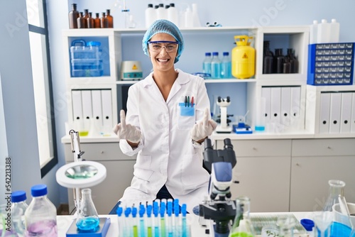 Brunette woman working at scientist laboratory showing middle finger doing fuck you bad expression  provocation and rude attitude. screaming excited