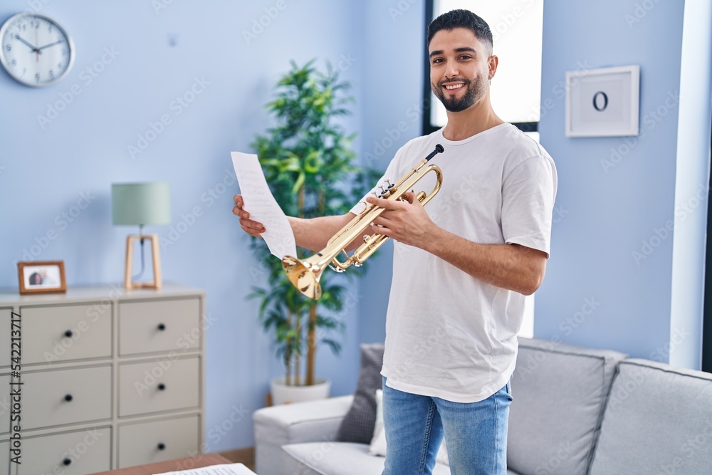 Young arab man musician holding trumpet and music sheet at home