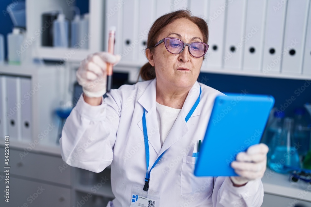 Senior woman scientist using touchpad holding blood test tube at laboratory Senior woman scientist using touchpad holding blood test tube at laboratory