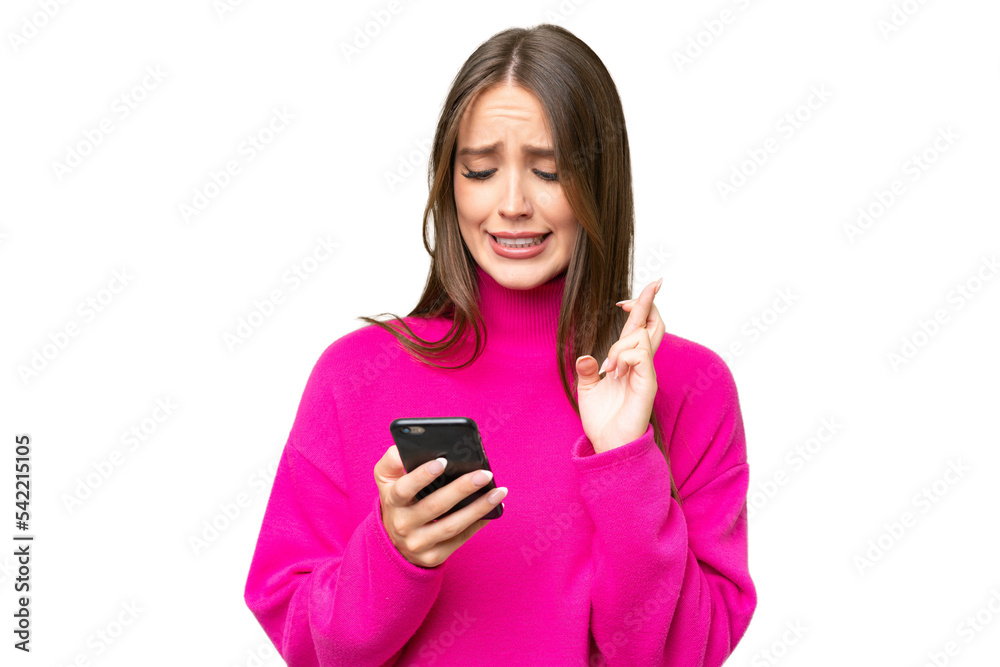 Young beautiful caucasian woman over isolated background using mobile phone with fingers crossing Young beautiful caucasian woman over isolated background using mobile phone with fingers crossing