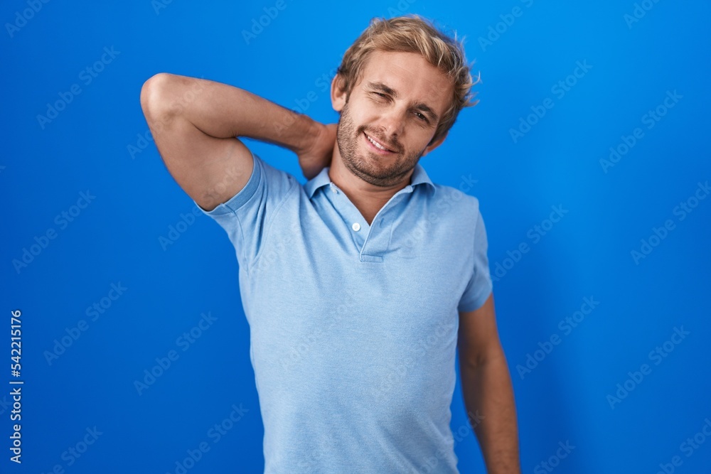 Caucasian man standing over blue background suffering of neck ache injury, touching neck with hand, muscular pain Caucasian man standing over blue background suffering of neck ache injury, touching neck with hand, muscular pain
