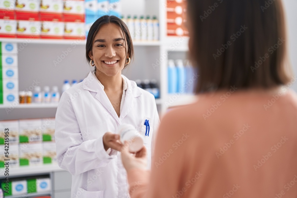 Two women pharmacist and customer holding pills bottle at pharmacy