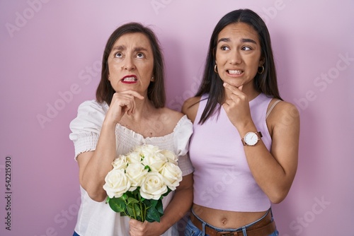 Hispanic mother and daughter holding bouquet of white flowers thinking worried about a question, concerned and nervous with hand on chin