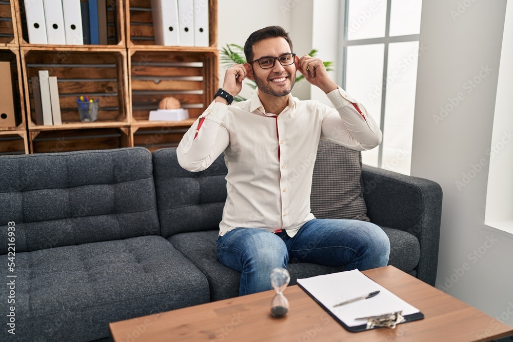 Young hispanic man with beard working at consultation office smiling pulling ears with fingers, funny gesture. audition problem Young hispanic man with beard working at consultation office smiling pulling ears with fingers, funny gesture. audition problem