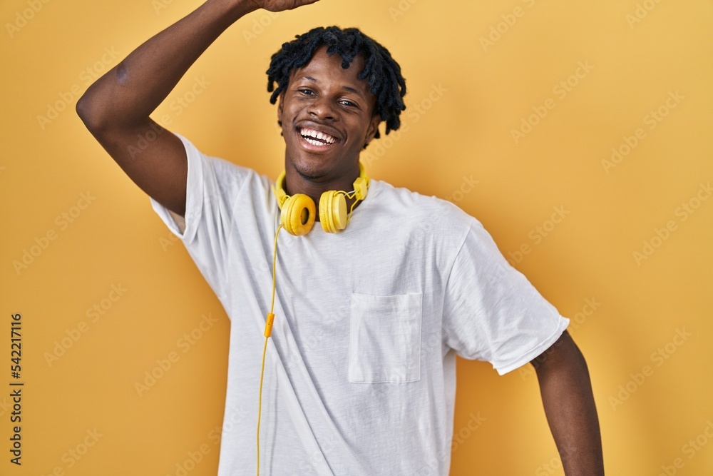 Young african man with dreadlocks standing over yellow background dancing happy and cheerful, smiling moving casual and confident listening to music