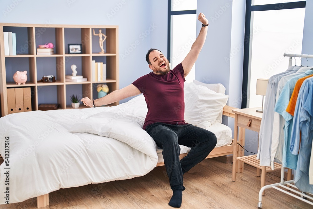 Young hispanic man waking up sitting on bed at bedroom Young hispanic man waking up sitting on bed at bedroom
