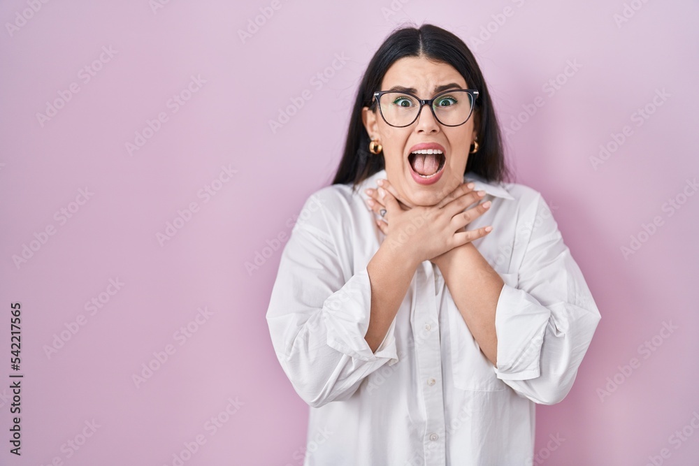 Young brunette woman standing over pink background shouting and suffocate because painful strangle. health problem. asphyxiate and suicide concept. Young brunette woman standing over pink background shouting and suffocate because painful strangle. health problem. asphyxiate and suicide concept.