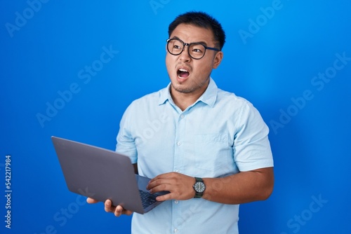 Chinese young man using computer laptop angry and mad screaming frustrated and furious, shouting with anger. rage and aggressive concept.