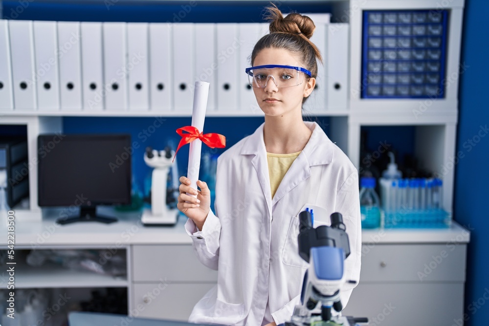Teenager girl working at scientist laboratory holding degree thinking attitude and sober expression looking self confident
