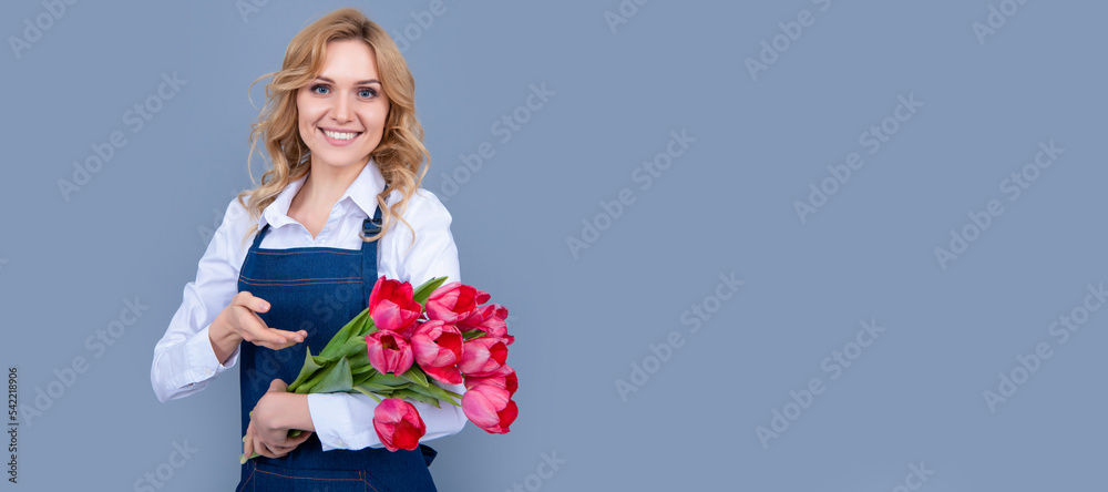 smiling girl in apron with spring tulip flowers on grey background. Woman isolated face portrait, banner with mock up copy space. smiling girl in apron with spring tulip flowers on grey background. Woman isolated face portrait, banner with mock up copy space.