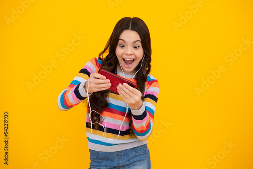 Amazed teenager use smart phone, share social media, chatting by mobile phone wear stylish casual trendy clothes isolated over yellow background. Child with smartphone. Excited teen girl.
