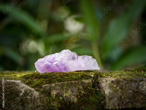Selective focus shot of a purple amethyst crystal mineral on a mossy rock surface