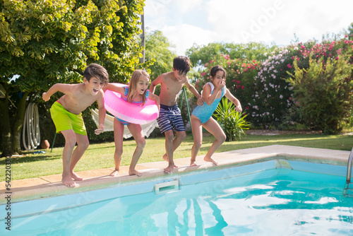 Portrait of four smiling children jumping into swimming pool. Happy Caucasian boys and girls in swimwear getting ready to jump into warm clear water. Leisure activity and kids healthy rest concept © KAMPUS