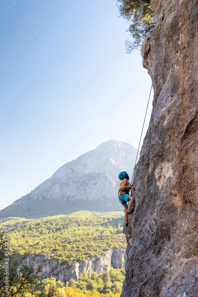 Obraz premium Children's rock climbing. The boy climbs a rock against the backdrop of mountains. Extreme hobby. An athletic child trains to be strong.