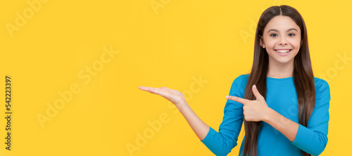 happy child with long hair presenting product and point finger on copy space, advertisement. Child face, horizontal poster, teenager girl isolated portrait, banner with copy space.