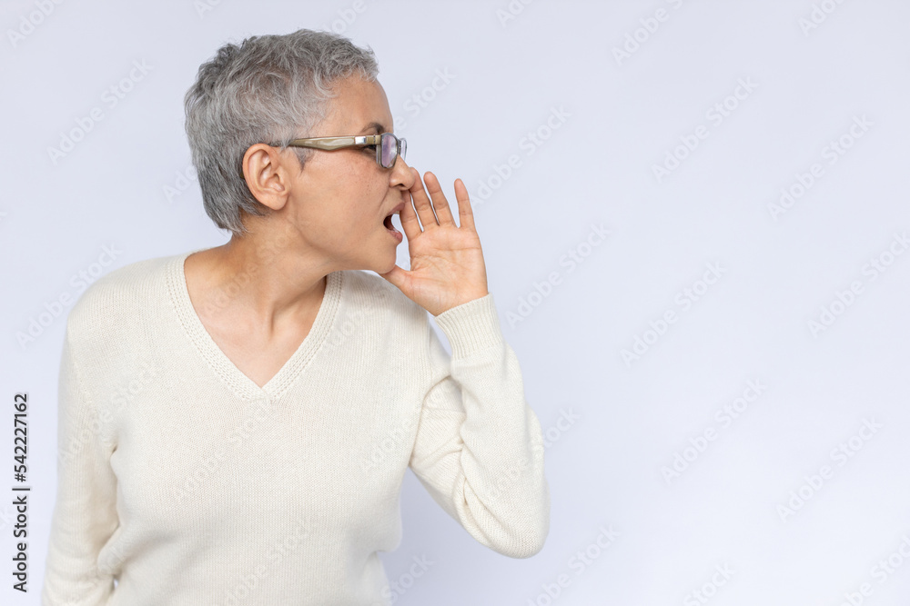 Portrait of confident senior woman shouting with hand at mouth. Mature Caucasian woman wearing eyeglasses and white jumper looking away and making announcement. Advertising concept Portrait of confident senior woman shouting with hand at mouth. Mature Caucasian woman wearing eyeglasses and white jumper looking away and making announcement. Advertising concept
