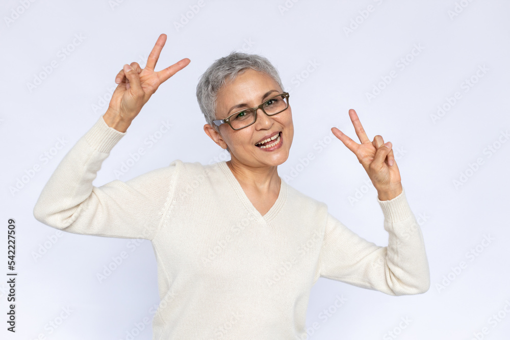 Portrait of cheerful senior woman making peace gesture. Mature Caucasian woman wearing eyeglasses and white jumper showing victory sign and smiling. Fun and happiness concept Portrait of cheerful senior woman making peace gesture. Mature Caucasian woman wearing eyeglasses and white jumper showing victory sign and smiling. Fun and happiness concept