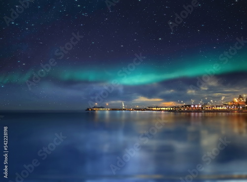 Night city blurred light on horizon at sea blue water wave and Aurora borealis on starry sky