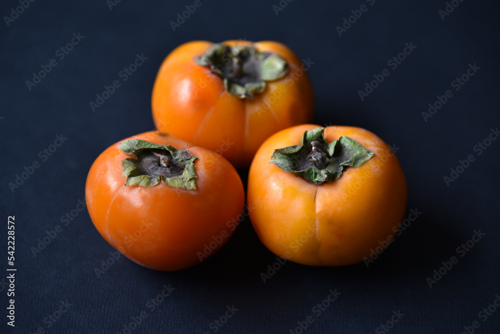 Orange persimmon fruits on a black background. Ripe and juicy persimmon fruits close-up. Orange persimmon fruits on a black background. Ripe and juicy persimmon fruits close-up.