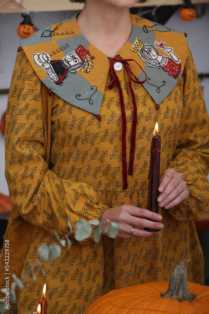 Fototapeta premium Fashion woman, girl in dress with patchwork collar. Embroidered collar. Halloween style, look, outfit. Decor with candles and pumpkins. Halloween decoration at home, indoor. Autumn Halloween decor