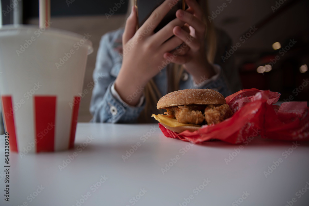 A young girl holds a phone in her hands while having lunch in a cafe. The concept of junk food, fast food