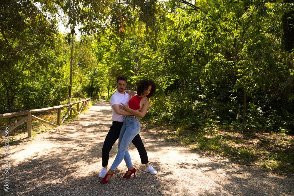 Handsome young man and woman dancing bachata and salsa in the park. The couple dance passionately surrounded by greenery. Dancing concept. Handsome young man and woman dancing bachata and salsa in the park. The couple dance passionately surrounded by greenery. Dancing concept.