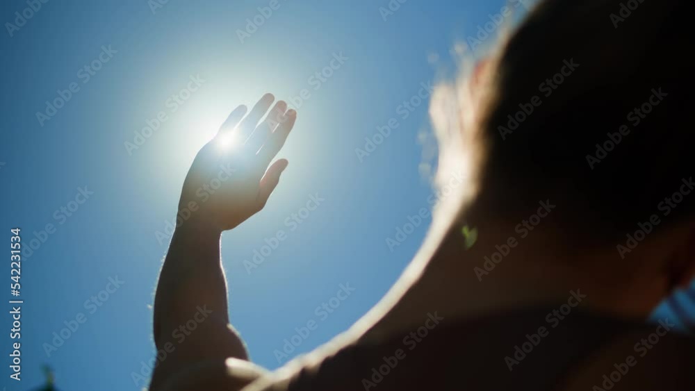 Woman closing sun by hand, blue sky, covering sunlight with arm. Young person looking at bright light.