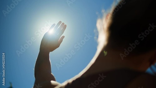Woman closing sun by hand, blue sky, covering sunlight with arm. Young person looking at bright light.