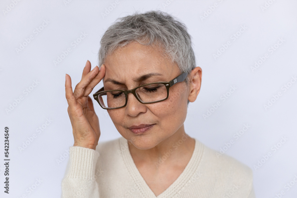 Close-up of stressed senior woman rubbing forehead. Mature Caucasian woman wearing eyeglasses and white jumper suffering from headache. Stress and migraine concept Close-up of stressed senior woman rubbing forehead. Mature Caucasian woman wearing eyeglasses and white jumper suffering from headache. Stress and migraine concept