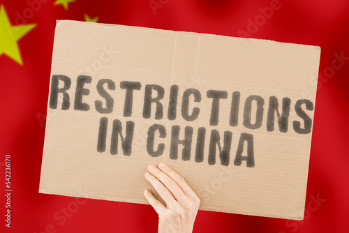 The phrase " Restrictions in China " is on a banner in men's hands with blurred background. Sanction. Conflict. Control. Independence. Law. Military. Password. Protection. Protest. Speak. Speech. War