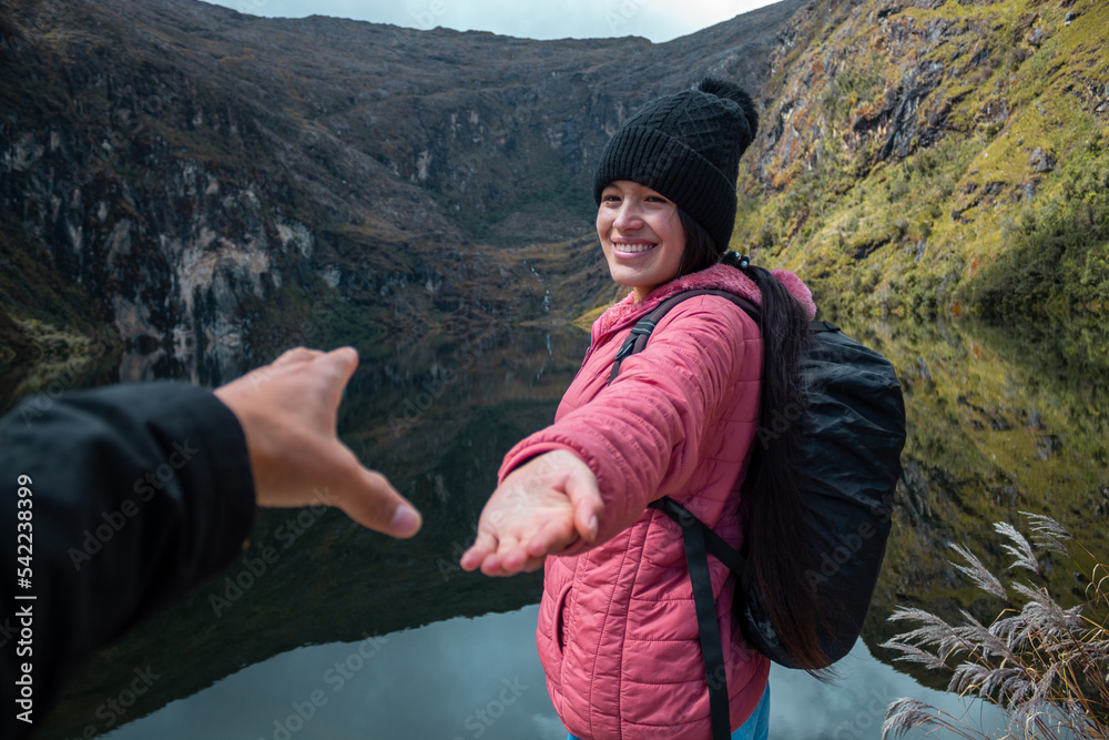 Hermoso excursionista sosteniendo una mano junto a un lago tranquilo en las montañas siempre verdes