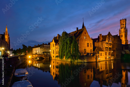 Famous view of Bruges tourist landmark attraction - Rozenhoedkaai canal with Belfry and old houses along canal with tree in the night. Brugge  Belgium