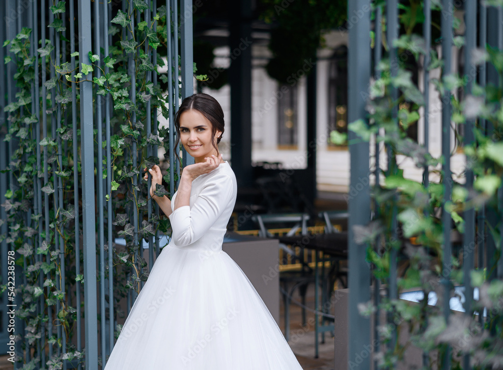 Portrait of smiling pretty young bride girl posing alone in long puffy white wedding dress outdoors. Attractive caucasian lady. Wedding model portrait. Dreamily bride woman