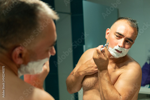 Close-up of a man shaving in front of a bathroom mirror photo