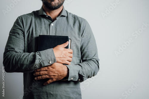 Standing man holding and hugging the bible on his chest.