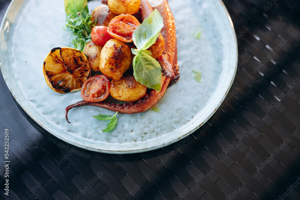 Φωτογραφία Grilled octopus tentacles with cherry tomatoes and baked baby potatoes in a blue porcelain plate on a black background