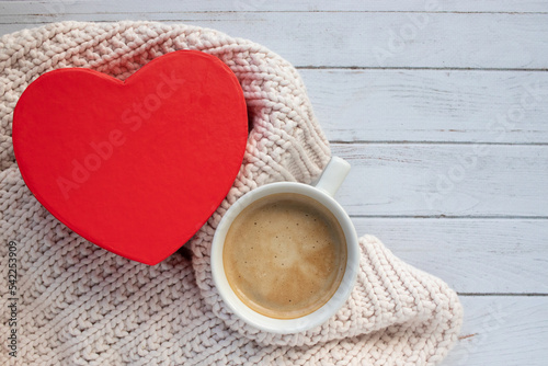 Cup of coffee with red heart shaped gift box and sweater on wooden table. Cappuccino mug, present, plaid on white background. Valentines day, Birthday, Mothers day. Top view, flat lay, copy space