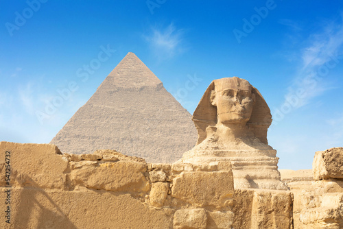 Egyptian Great Sphinx full body portrait with head  feet with all pyramids of Menkaure  Khafre  Khufu in background on a clear  blue sky day in Giza  Egypt empty with nobody.