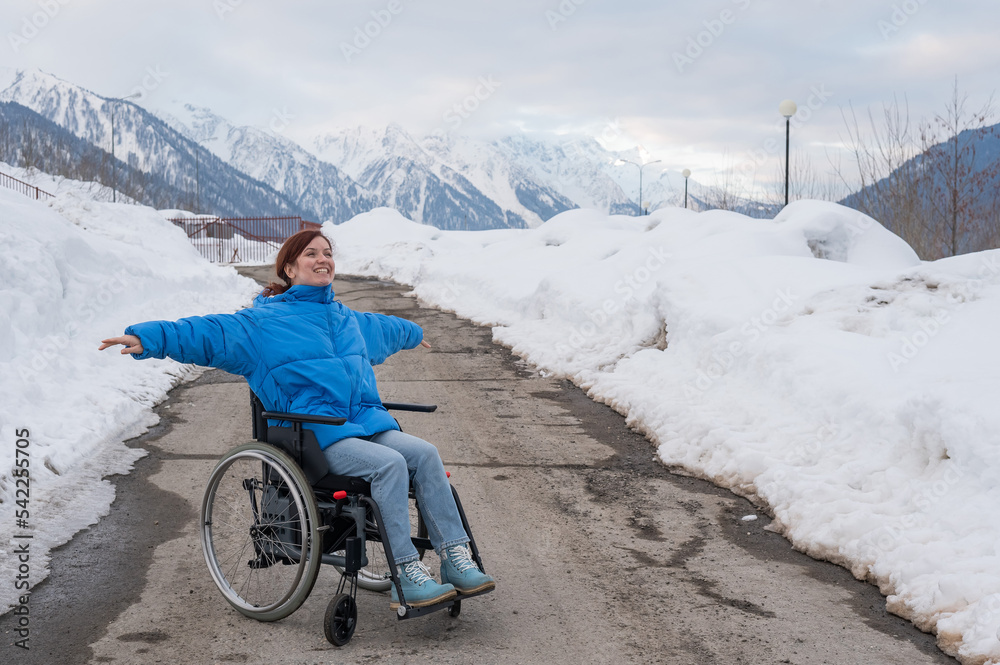 A woman in a wheelchair spread her arms to the side like wings in the mountains in winter.