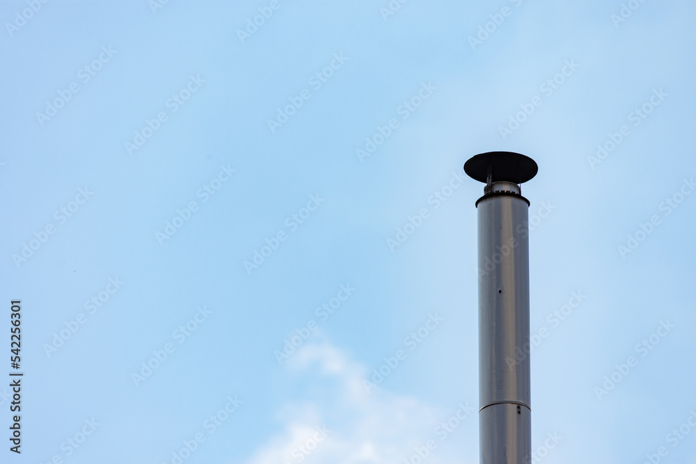 Metallic chimney pipe with cowl for rain protection on a roof against blue sky Metallic chimney pipe with cowl for rain protection on a roof against blue sky