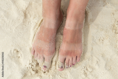 Funny tanned legs on the white sand beach. Women's feet with uneven tan. The concept of skin protection from the sun.