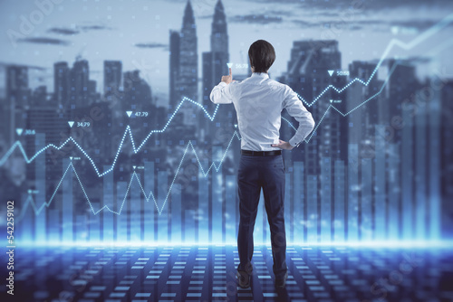 Photos Attractive young european business man with abstract glowing blue business graph hologram on blurry city background