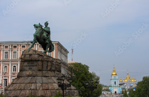 A sculpture of Hetman of Ukraine Bohdan Khmelnytskyi riding a horse against the background of a blue church with golden domes. The historical center of Kyiv. Bronze sculpture of an outstanding histori