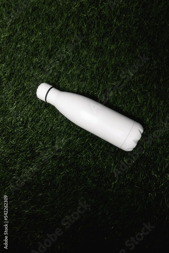 White stainless thermo bottle isolated on green grass. Reusable bottle saves the environment. Ecology