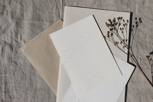 Christmas office supply. Holiday stationery. Blank greeting card, invitation and diary mockups. Craft envelope and dry grass in sunlight. Beige linen tablecloth. Winter wedding flat lay, top view