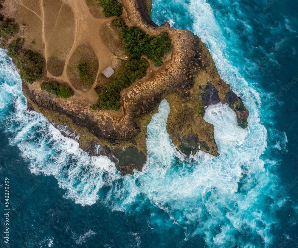 Aerial top view of waves crashing the coast of an island