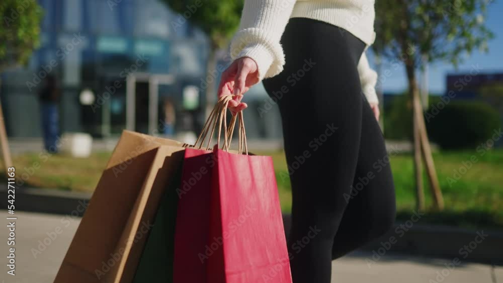 Close up of woman walking with shopping bags in hands in city from mall. Low angle view of girl going with purchases from black friday sale. Female with full paper bags. Slow motion.