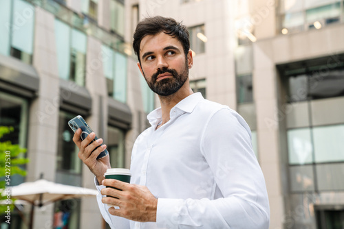 White man using mobile phone and drinking coffee at city street