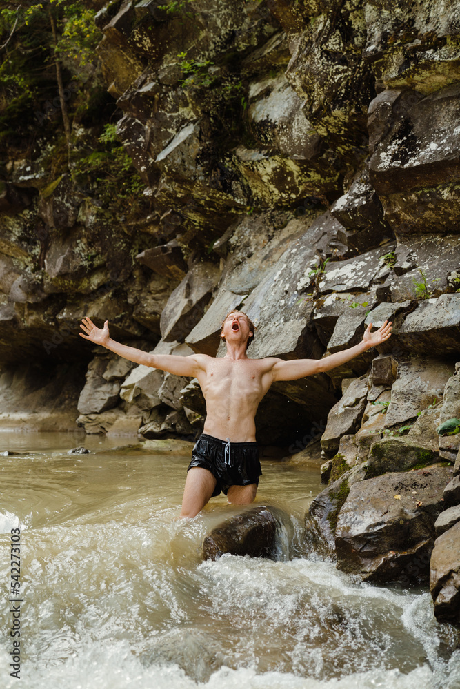 White young man wearing swimming trunks standing in mountain river White young man wearing swimming trunks standing in mountain river