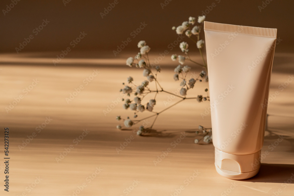 Unbranded white squeeze cosmetic cream bottle tube and dry gypsophila flower on beige background with harsh shadows. Natural oranic spa cosmetics concept. Mockup, template, front view Unbranded white squeeze cosmetic cream bottle tube and dry gypsophila flower on beige background with harsh shadows. Natural oranic spa cosmetics concept. Mockup, template, front view